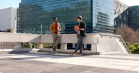 Diverse young men chatting on urban rooftop terrace holding basketball in sunlight