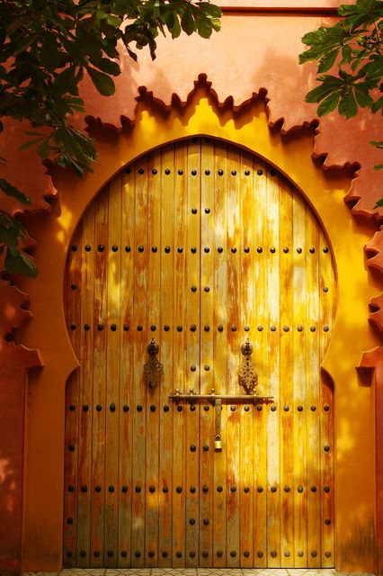 Vintage wooden door with ornate archway reflecting Moroccan architectural style. Image features vibrant yellow hues, intricate detailing, and brass lock. Ideal for use in travel articles, cultural blogs, architectural magazines, and design inspiration.