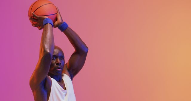 Image of african american male basketball player throwing ball on pink to orange background. Sports and competition concept.
