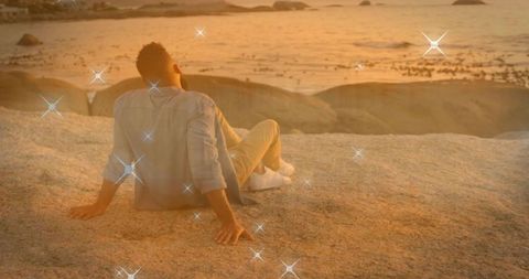 Man gazing at sunset over rocky coastline with sparkling golden glow