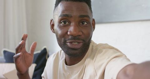 Young black man recording casual vlog on living room couch gesturing and talking
