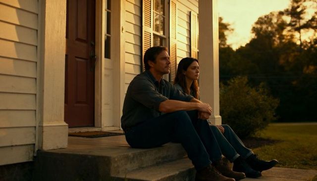 Couple sitting on porch steps at sunset gazing across yard, rural calm moment