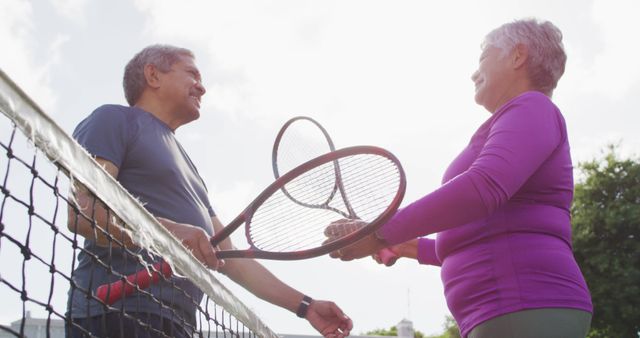 Senior adults enjoying a game of tennis outdoors, holding tennis rackets, and smiling at each other. Perfect for illustrating concepts of active lifestyle, senior fitness, sportsmanship, healthy living, and outdoor recreation.