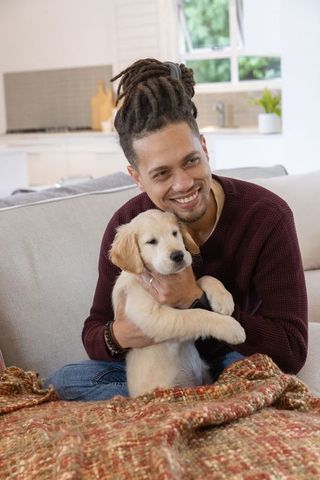 Smiling african american man cuddling golden retriever puppy on sunlit cozy sofa
