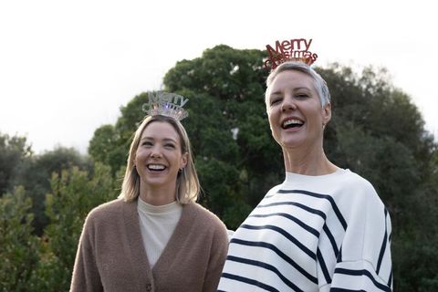 Two women laughing outdoors wearing merry christmas headbands celebrating family holiday
