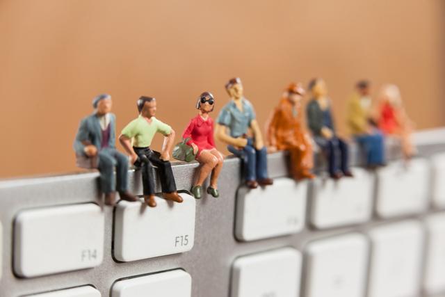 Miniature figures sitting on a computer keyboard, representing teamwork, creativity, and digital collaboration. Ideal for illustrating concepts related to technology, business, innovation, and office environments. Can be used in marketing materials, websites, and presentations to convey themes of teamwork and modern workspaces.