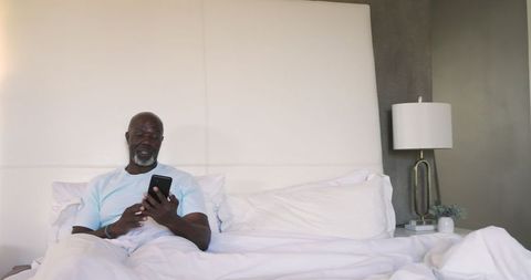 Senior Man Engaging with Smartphone While Relaxing in Bed