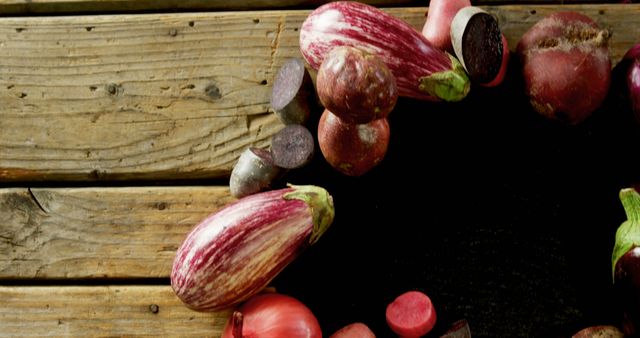 Colorful assortment of fresh organic vegetables including eggplants and radishes laid out on a rustic wooden table. Ideal for farm-to-table culinary themes, organic food blogs, farmer's market promotions, and healthy eating posters.
