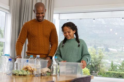 African american father and daughter sorting recycling and containers at bright home table
