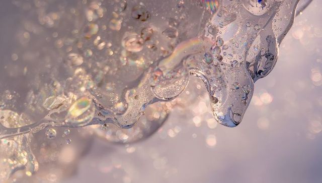 Iridescent melting ice macro showing rainbow prisms, crystal droplets and bokeh glow