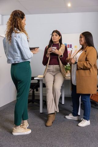Multicultural women collaborating and discussing project around modern office desk