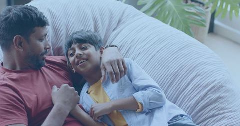 Father and Son Reclining on Pink Beanbag, Embracing and Smiling in Cozy Living Room