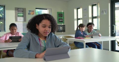 Teenage girls learning with tablets in bright classroom, collaborating and concentrating
