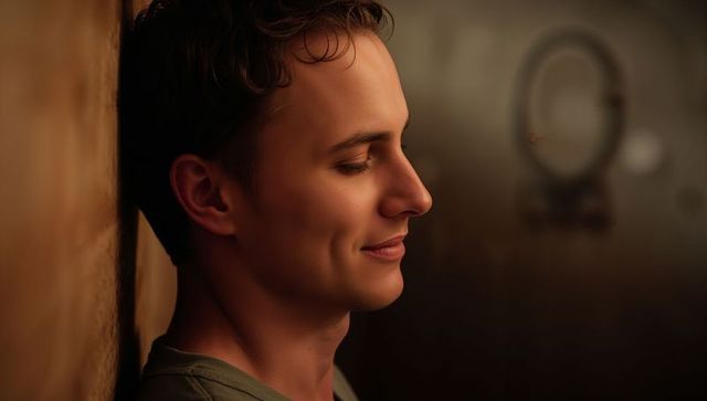 Young man leaning against textured wall, serene profile portrait with warm brown interior