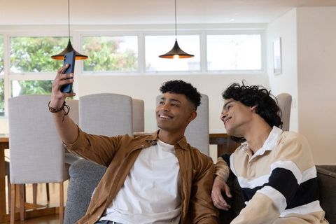 Teen friends taking selfie on couch, smiling in bright modern home interior, lifestyle