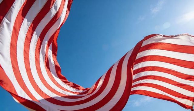Billowing american flags twisting across bright blue sky with sun flare