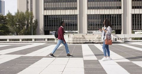 Young adults walking and checking phone on striped urban plaza tiles, city lifestyle