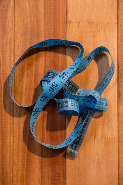 This image shows a blue measuring tape coiled on a wooden surface, ideal for use in articles or advertisements related to sewing, tailoring, crafting, or DIY projects. It can also be used in educational materials about measurement and accuracy.