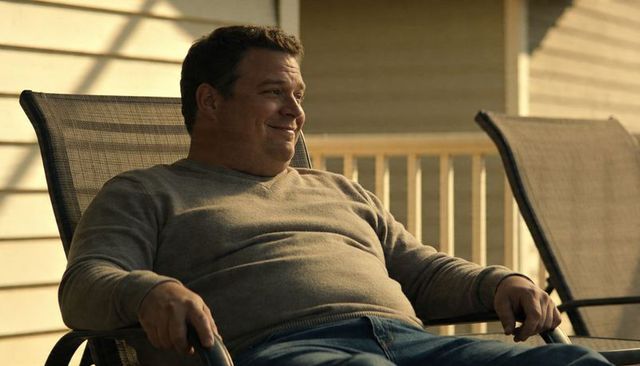 Relaxing man reclining on mesh patio chair on sunlit wooden porch wearing casual pullover