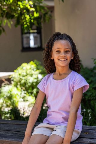 Smiling african american girl sitting on bench in sunlit courtyard garden
