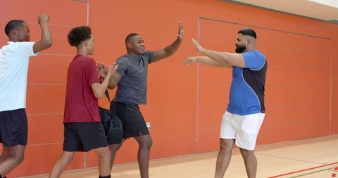 Multiethnic players celebrating on indoor court high-fiving teammates walking with duffel