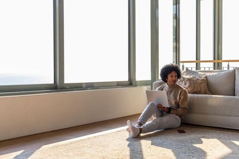 African american man working on laptop in sunlit loft apartment living room