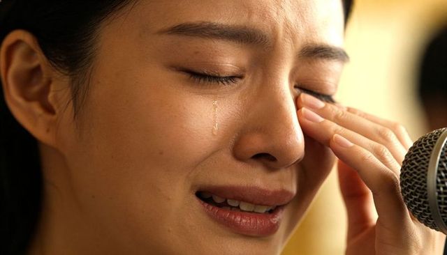 Asian singer crying closeup with tear rolling down cheek wiping eye at microphone