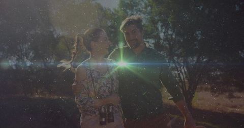 Couple walking on sunlit trail holding binoculars, laughing with cinematic lens flare