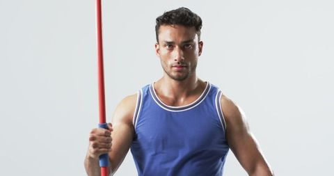 Determined male athlete holding javelin indoors