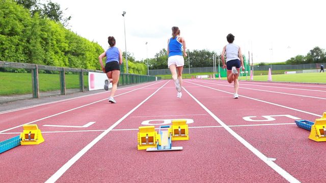 Women athletes use starting blocks as they sprint forward on a red track. Ideal for promoting athletic events, sportswear, fitness lifestyle and motivation in sporting advertising campaigns.