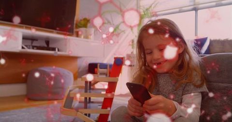 Young girl smiling and tapping smartphone in cozy living room play area with pink overlay