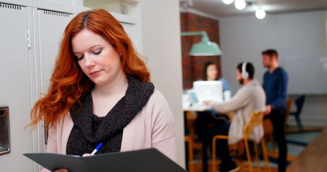 Woman Taking Notes with Colleagues Working in Background - Download Free Stock Images Pikwizard.com