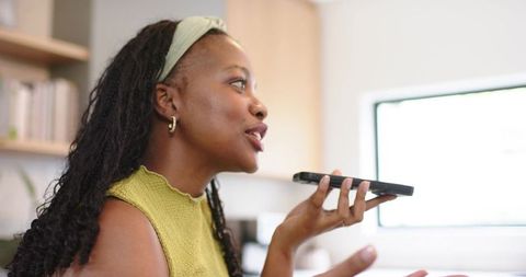 African American woman speaking into smartphone while teleworking in bright home office