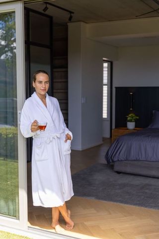 Morning calm: woman in white bathrobe standing at sliding door holding tea on doorstep