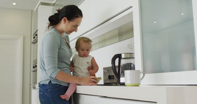 Caucasian mother holding her baby using smartphone in the kitchen at home. motherhood, love and childcare concept