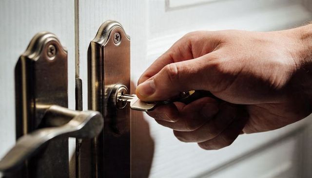 Male hand inserting key into brass home door lock closeup for residential security entry