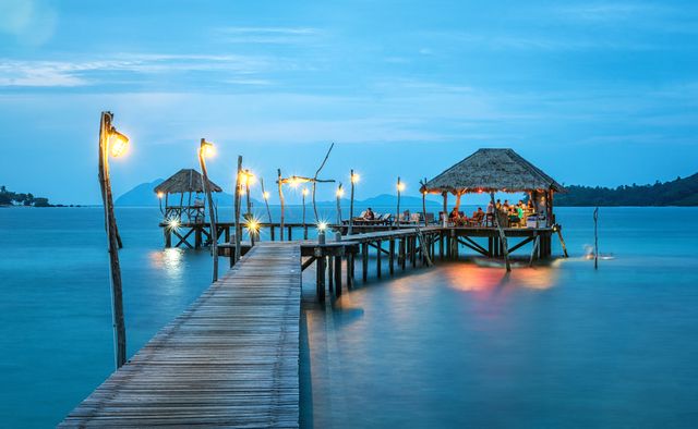 Tropical Pier with Lit Huts at Sunset over Serene Sea - Download Free Stock Images Pikwizard.com