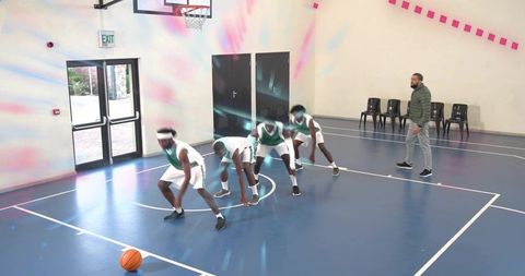 Youth basketball team practicing dribbling drill on blue indoor court with coach observing
