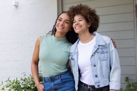 Smiling african american friends embracing on porch wearing casual denim and spring tops
