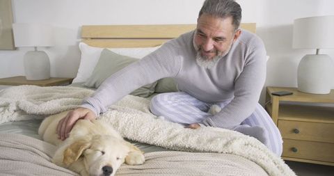 Senior man petting sleeping puppy in modern cozy bedroom