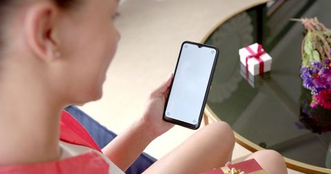 Teen Woman Holding Smartphone at Home with Gift Nearby