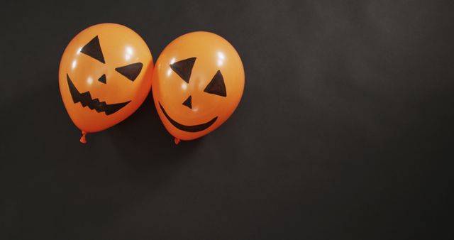 This image shows two orange balloons decorated like jack-o'-lanterns against a dark background. It is ideal for use in Halloween-themed promotions, advertisements, party invitations, and website banners to add a festive, spooky touch.