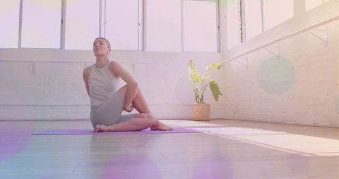 Practicing seated spinal twist in sunlit minimalist studio with purple mat