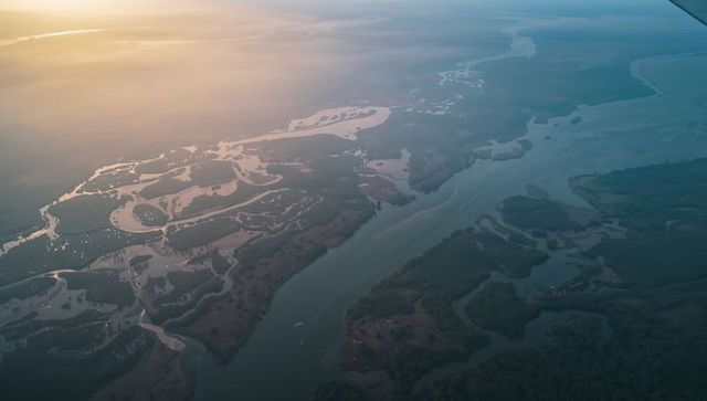 Golden-hour aerial showing meandering river and braided wetlands from small aircraft wing