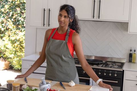 Woman chopping garlic on modern kitchen island wearing grey apron and red top cooking