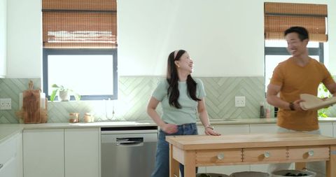 Laughing couple preparing meal at wooden island in bright modern farmhouse kitchen
