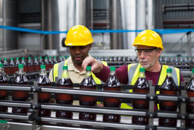 Factory workers monitoring drinks production line, ensuring quality control and efficiency. Ideal for use in articles about manufacturing processes, industrial safety, teamwork in factories, and beverage production.