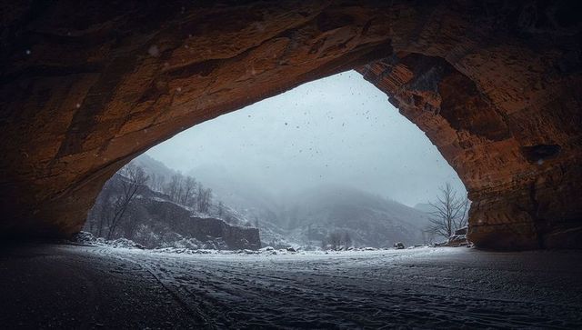 Framing cave arch revealing snow-covered valley and misty sandstone canyon in winter