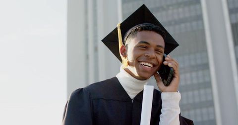 African american graduate smiling and calling on smartphone while holding diploma outdoors