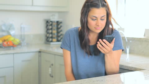 Woman Smiling While Using Smartphone in Modern Kitchen